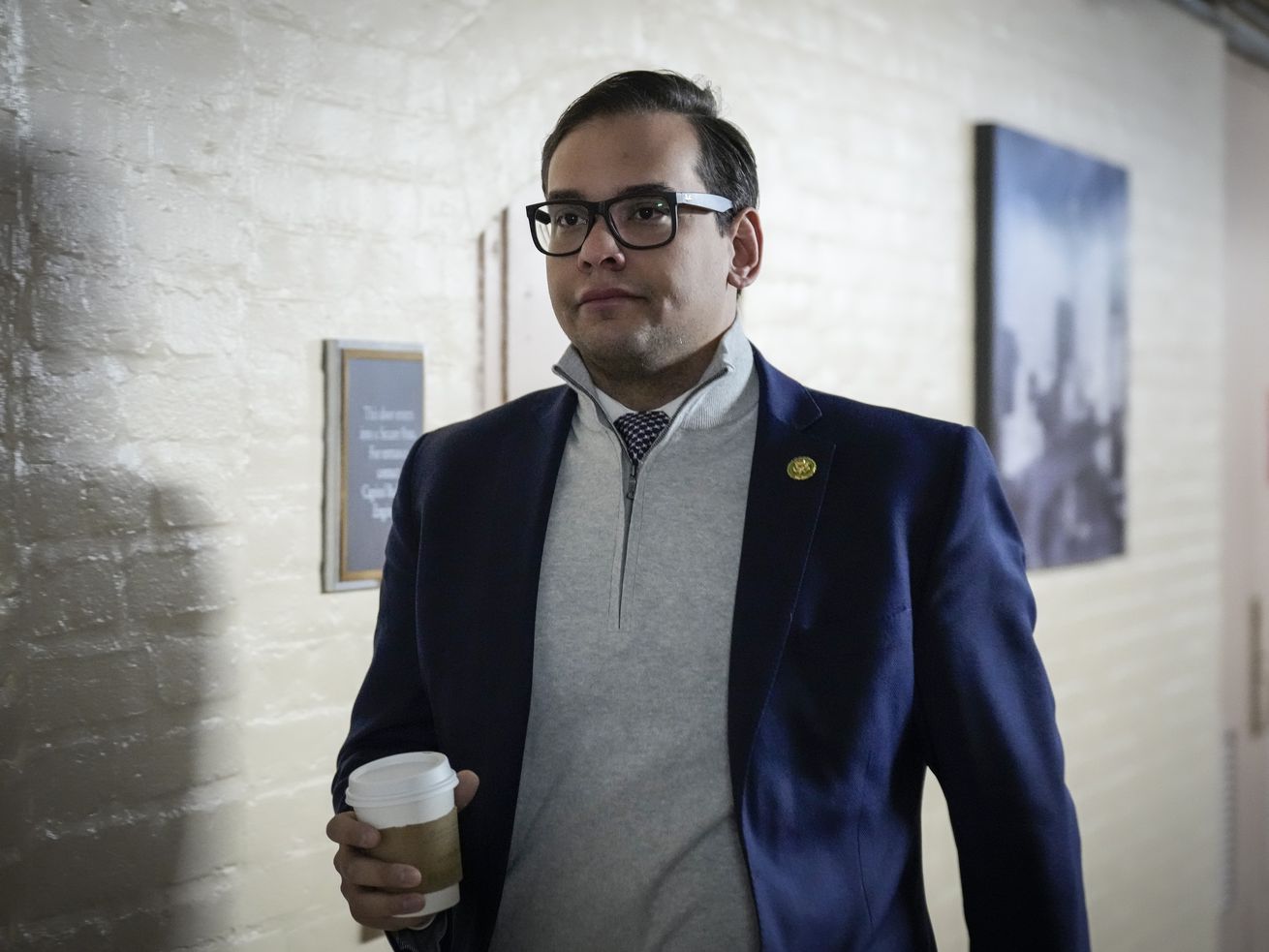 Rep. George Santos walks through a Capitol hallway with a to-go coffee cup in hand.