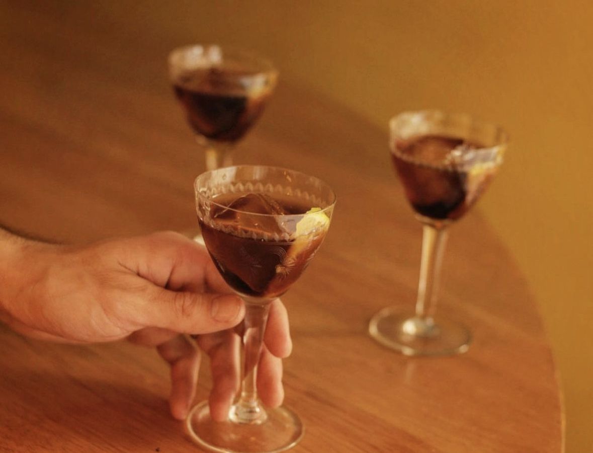 A hand holds a deep red cocktail, with two others nearby.