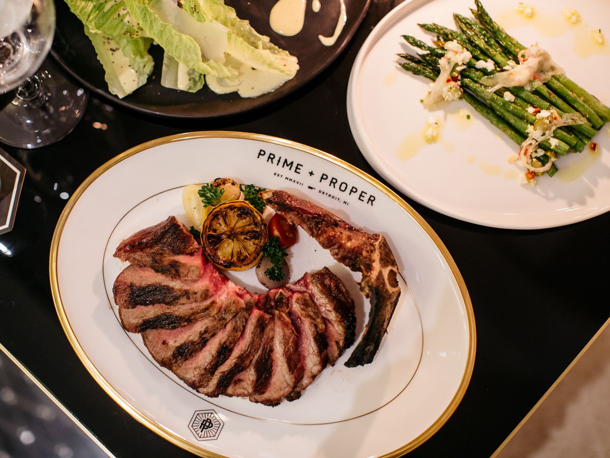 Several dishes including steak, asparagus, and romaine lettuce set on white plates with gold trim