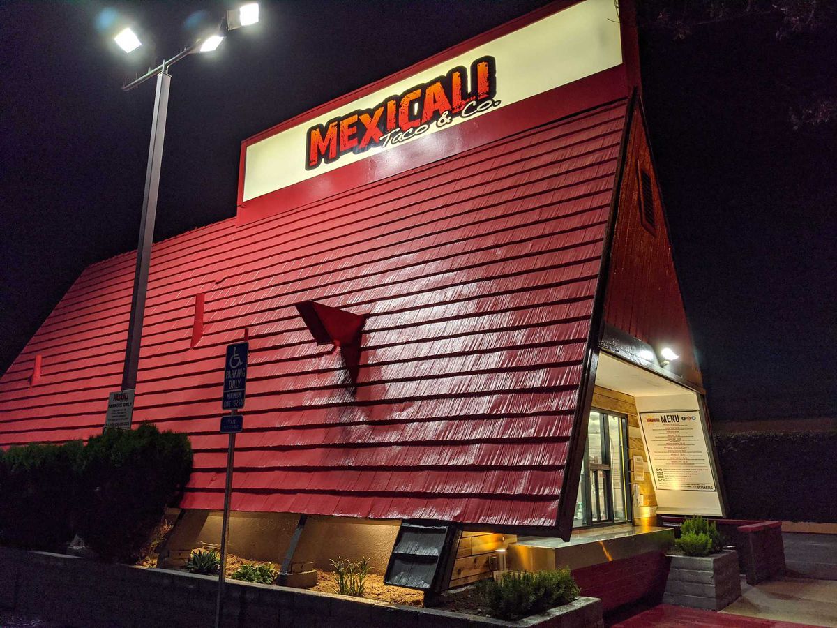 A pitched red roof with a sign for a taco restaurant, shown at night.