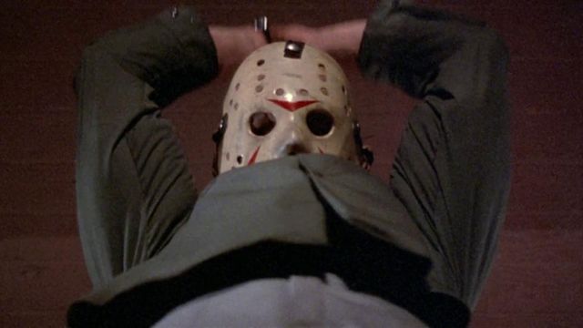 Jason Voorhees, wearing his signature hockey mask, holds both hands over his head about to slice somebody in Friday the 13th Part III.