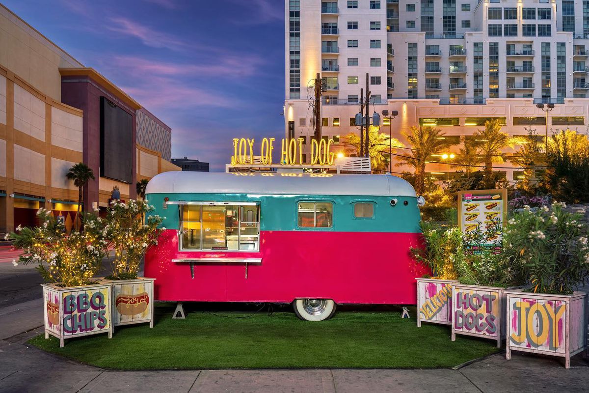 A neon lit, pink and aqua hot dog trailer
