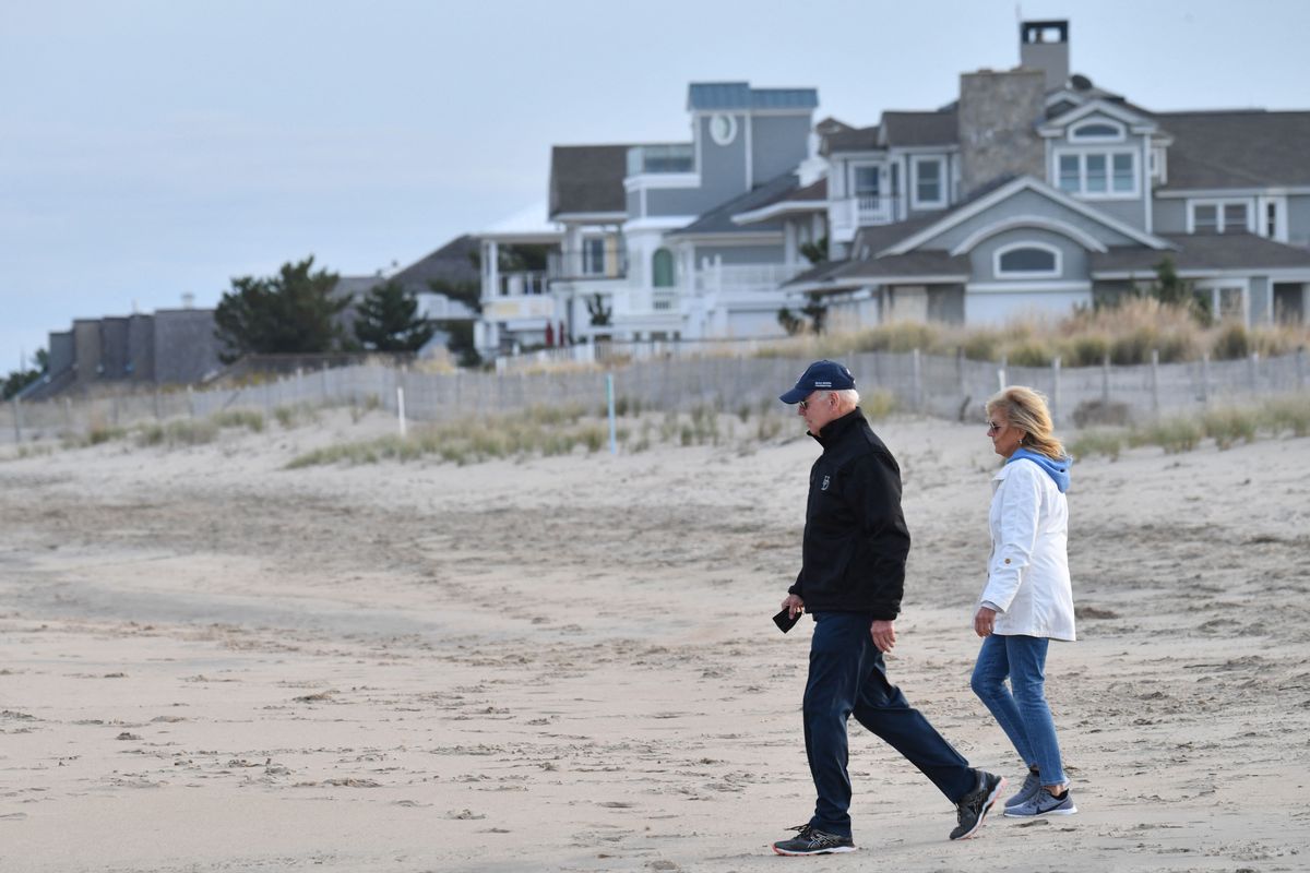 Joe and Jill Biden viewed in profile on a beach with homes in the background. 