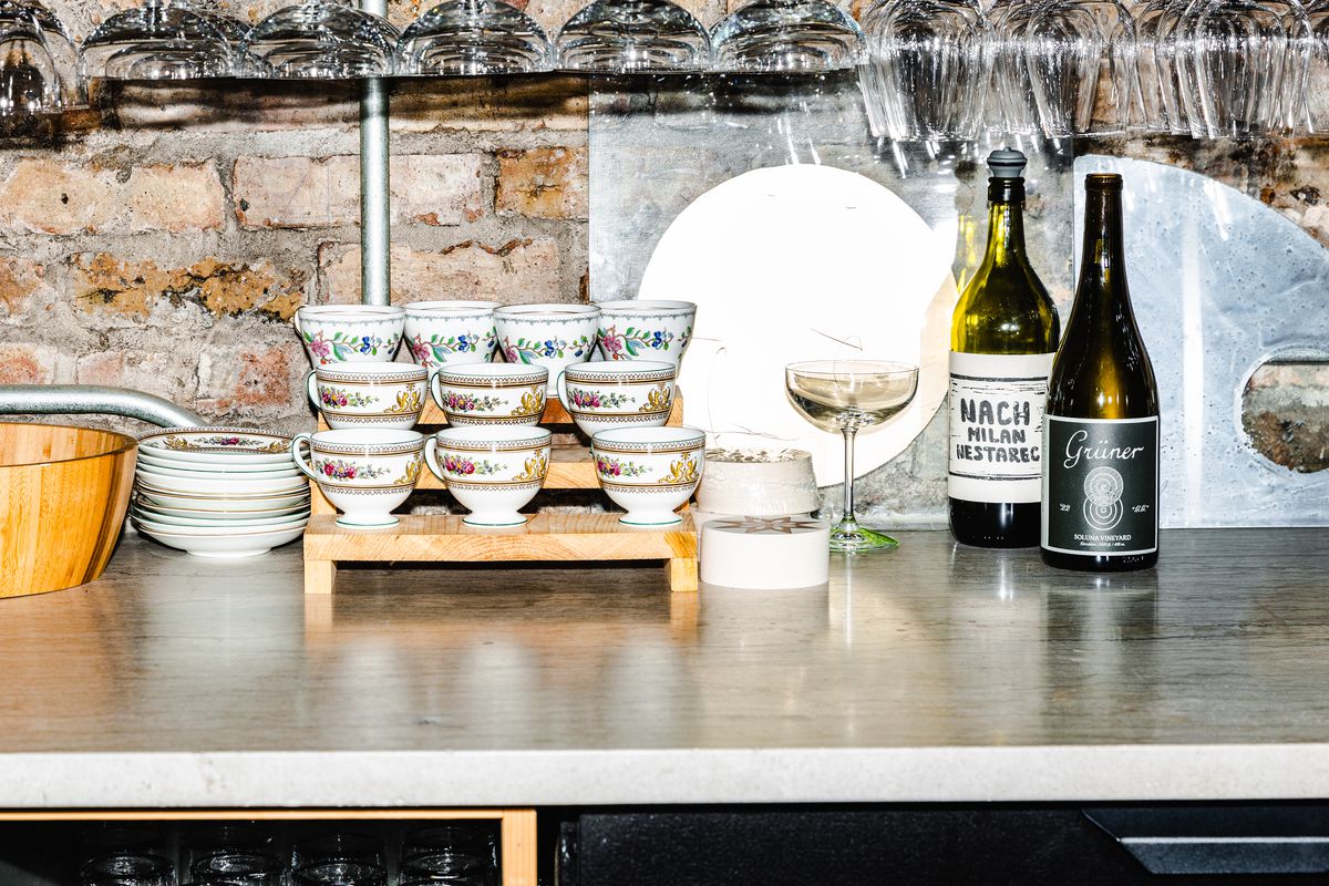 A counter holds a display of teacups beside two bottles of wine.