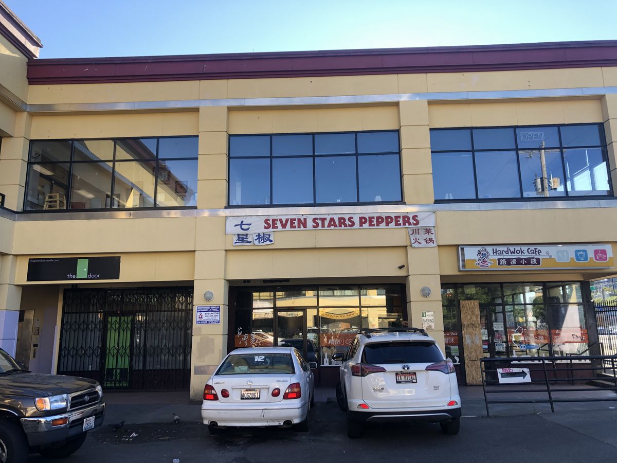 Part of a two-story shopping mall, with parking and a couple of restaurants on the first floor, and a sign reading “Seven Stars Pepper” under an empty restaurant space on the second.