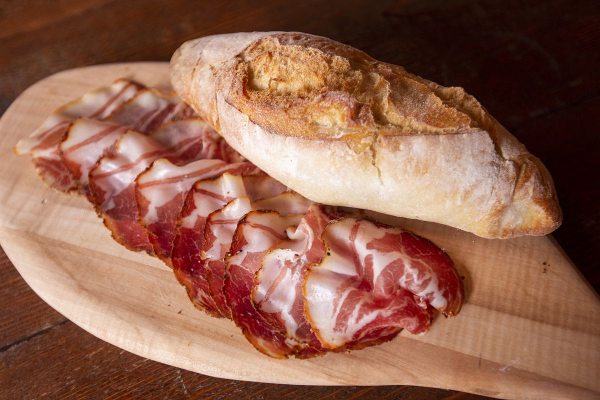 A wooden board holds sliced charcuterie and a small loaf of bread