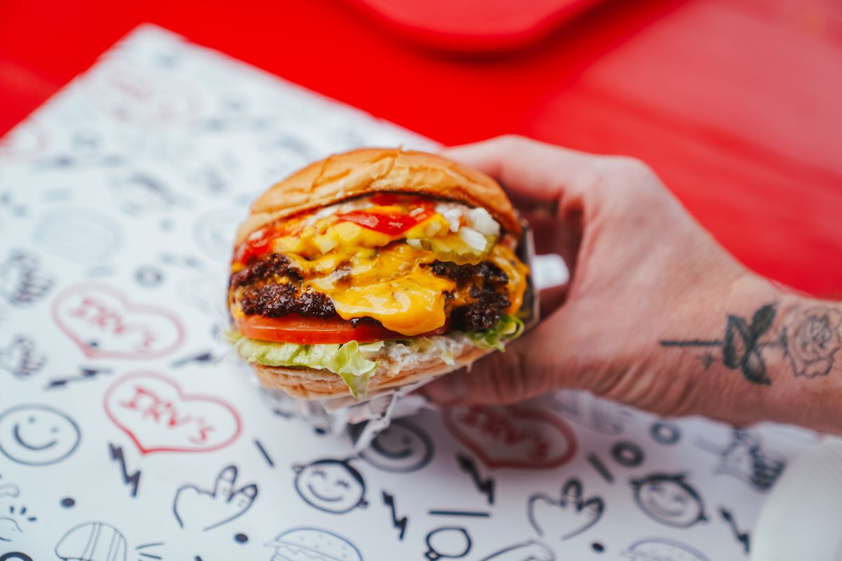 A cheesy burger on a paper covered in doodles. 