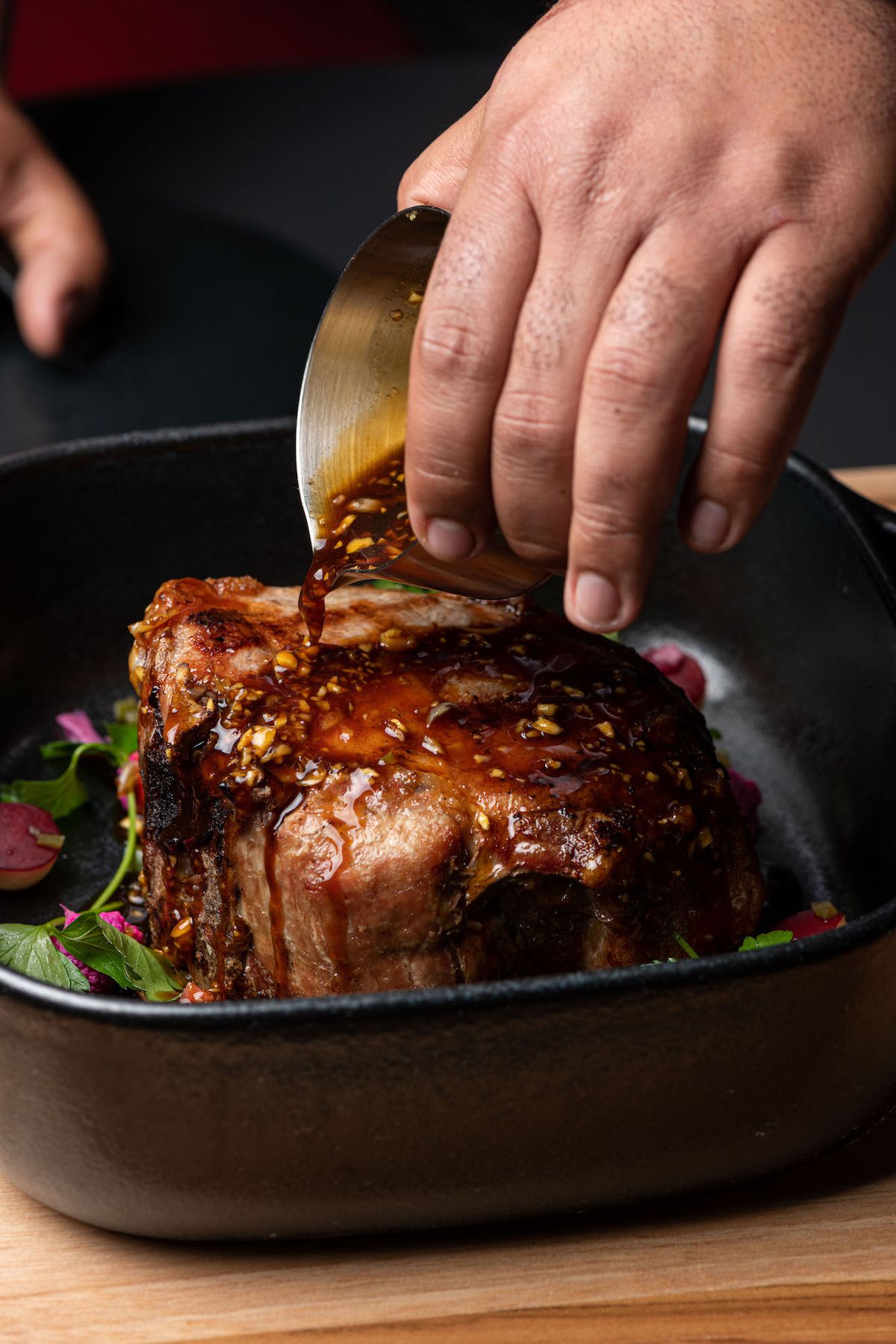 A server pours sauce over a thick pork chop tableside.