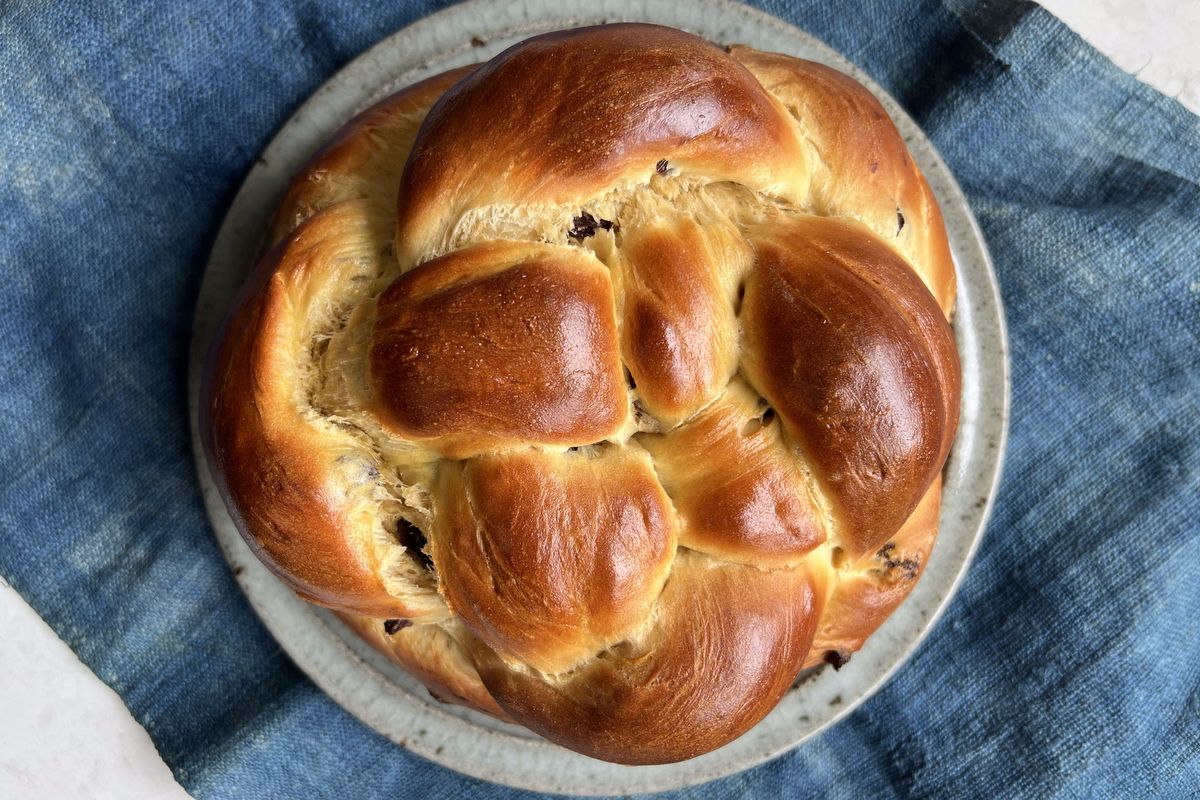 A round loaf of braided challah sitting on top of a plate and a blue napkin.