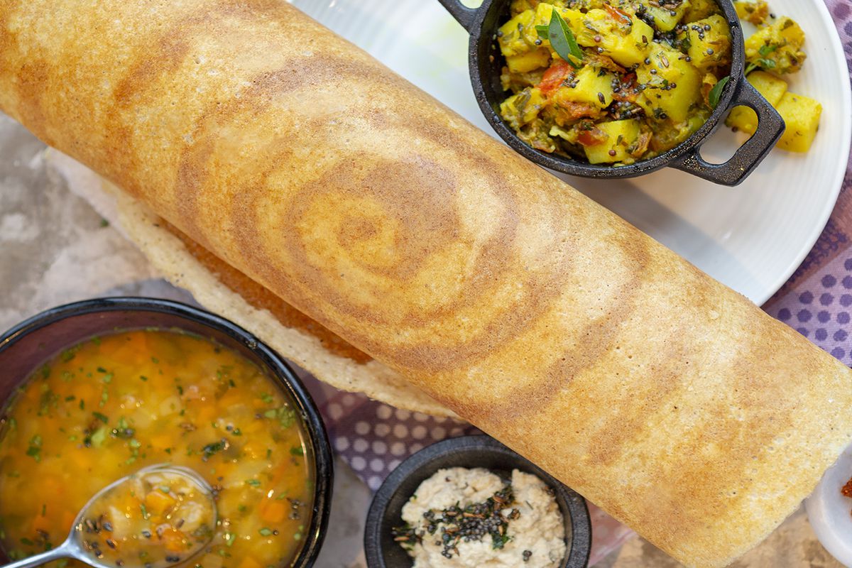 A plate with a dosa, sambar, and more.