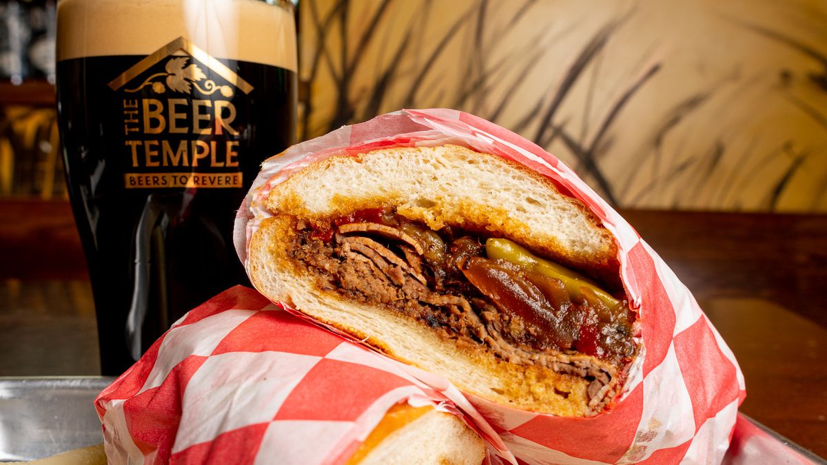 A beef sandwich and stout in a pint glass.
