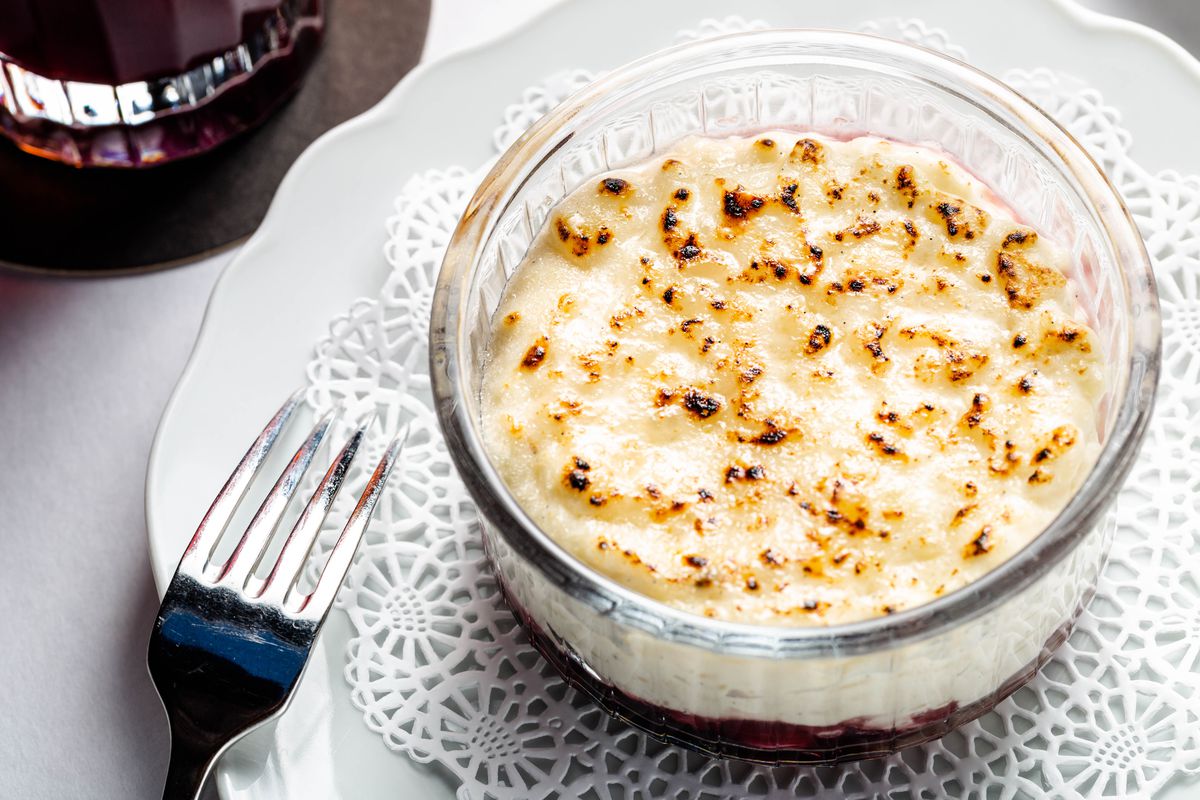 Bruleed white rice pudding sits in a glass ramekin over a purple concord grapes poached with red wine