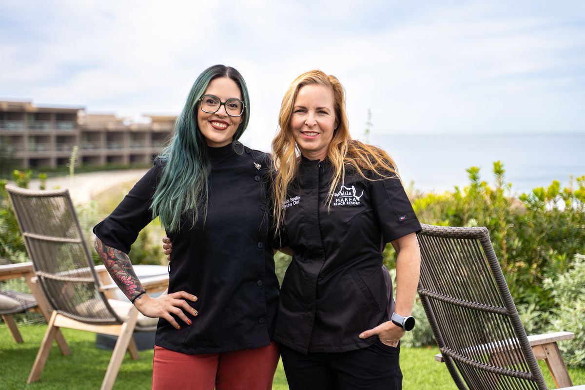Two female chefs pose together overlooking the ocean.