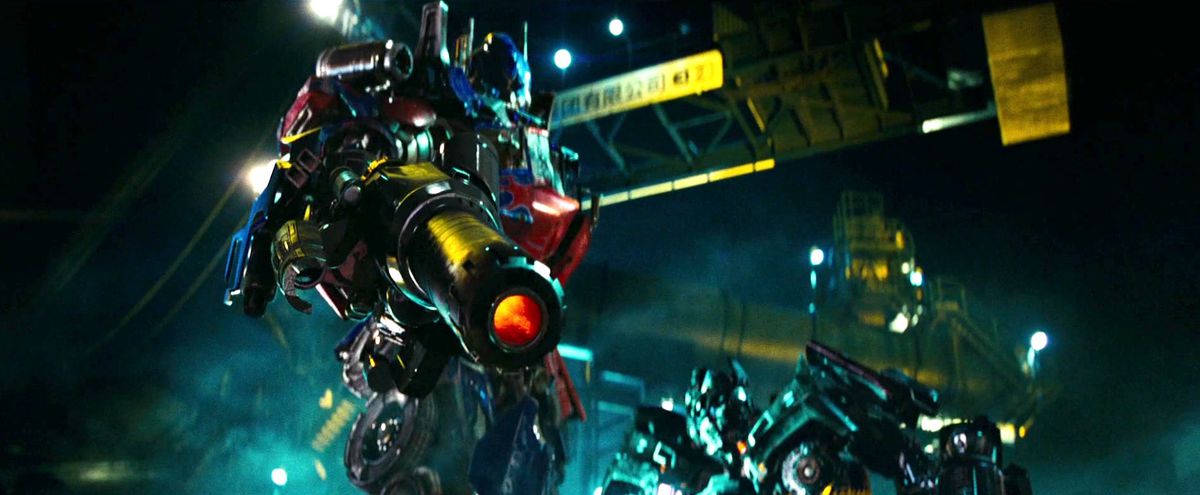 Optimus Prime holds up a gun and pulls the trigger while another Transformer watches in Revenge of the Fallen