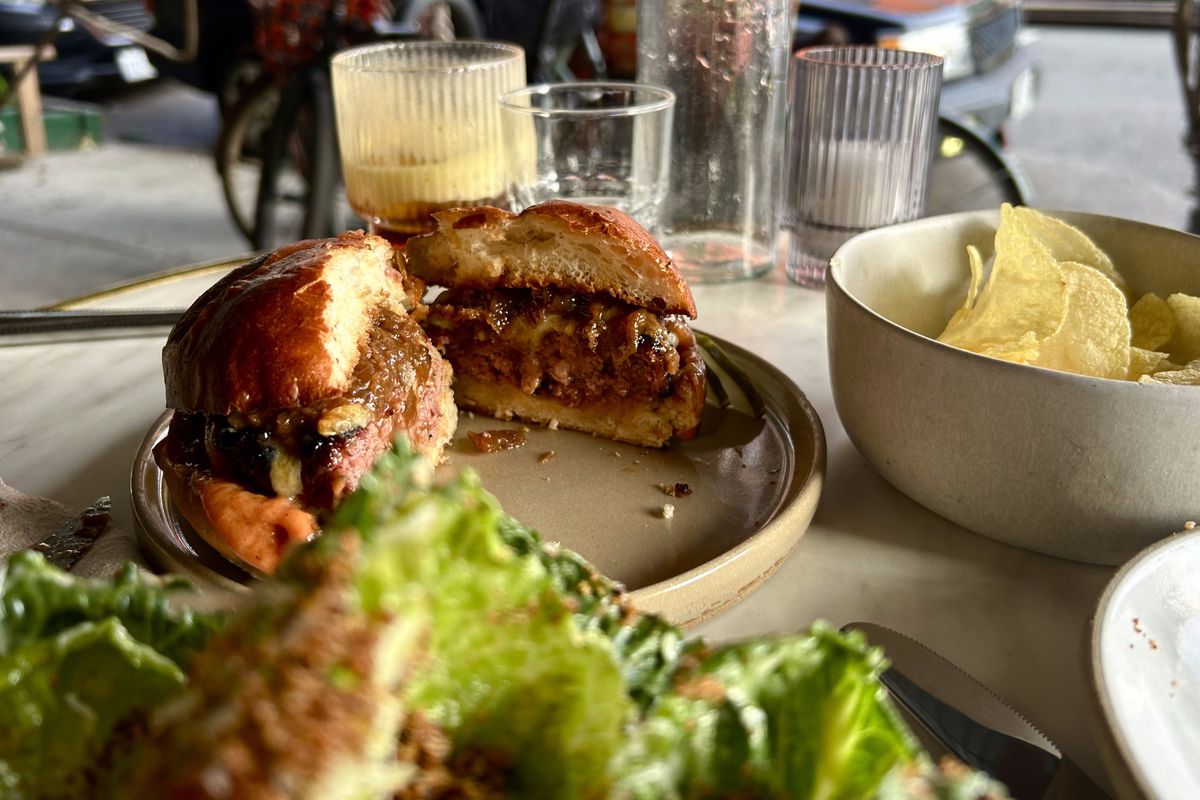 A burger sits on a brioche bun on a plate at an outdoor table.