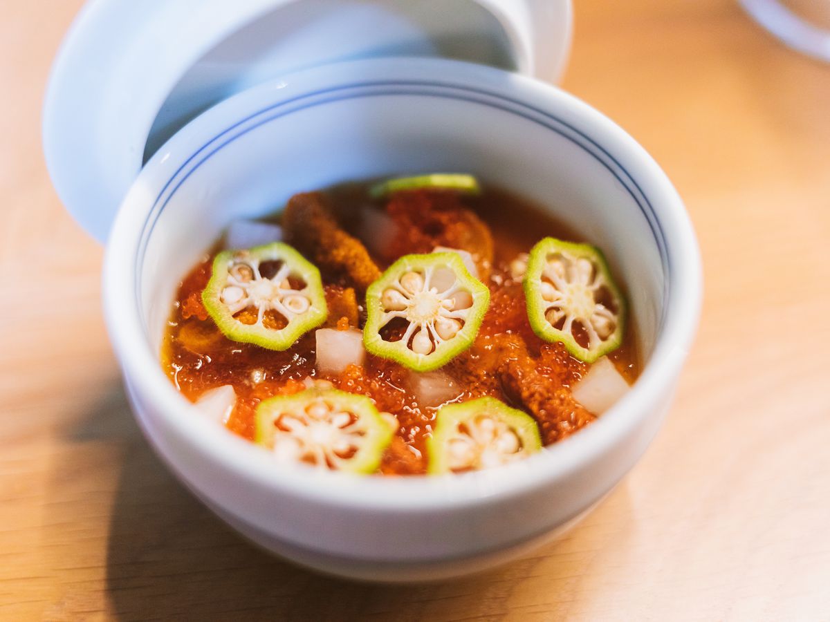 A ceramic bowl, a lid resting nearby, contains sea urchin and thin slices of spicy pepper
