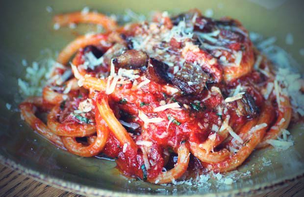 Closeup shot of thick pasta noodles covered in red sauce and grated parmesan cheese on a green ceramic plate.