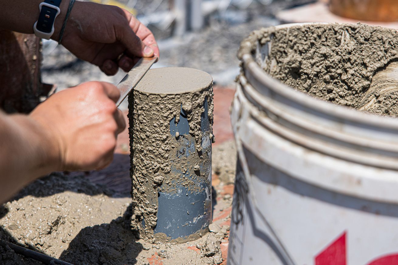 A worker uses a concrete smoother on top of a metal canister