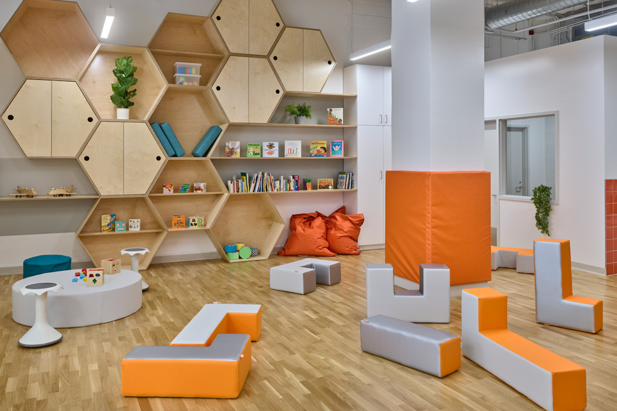 The interior of a daycare with orange bean baggies, cubbies filled with books, and plants.