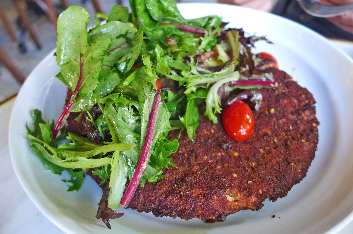 A breaded chicken cutlet peeks out from under an arugula and tiny tomato salad.