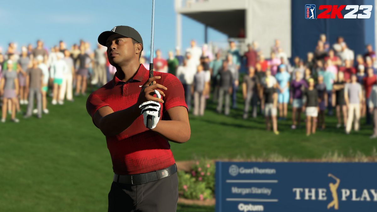 golfer Tiger Woods, wearing black slacks and a red and gray polo, watches a shot fly with a crowd of spectators behind him at The Players Championship in PGA Tour 2K23