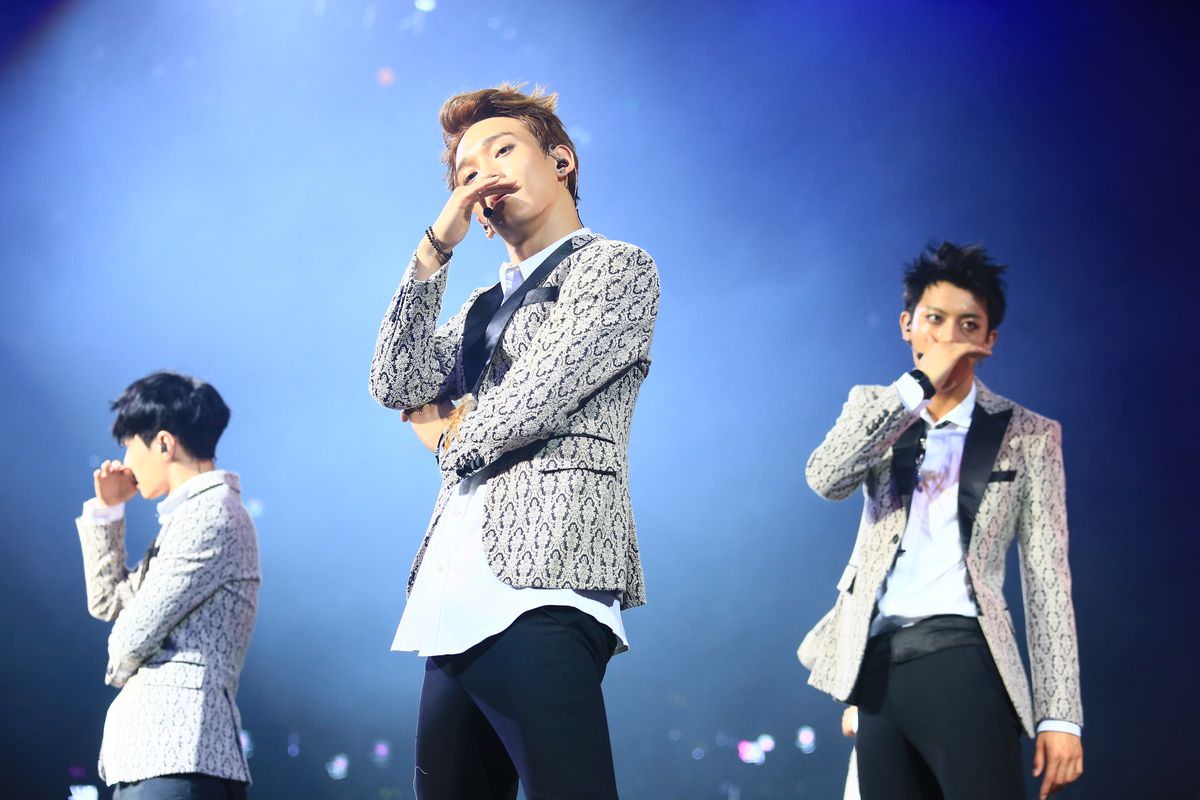 Three members of a Korean boy band pose on stage.