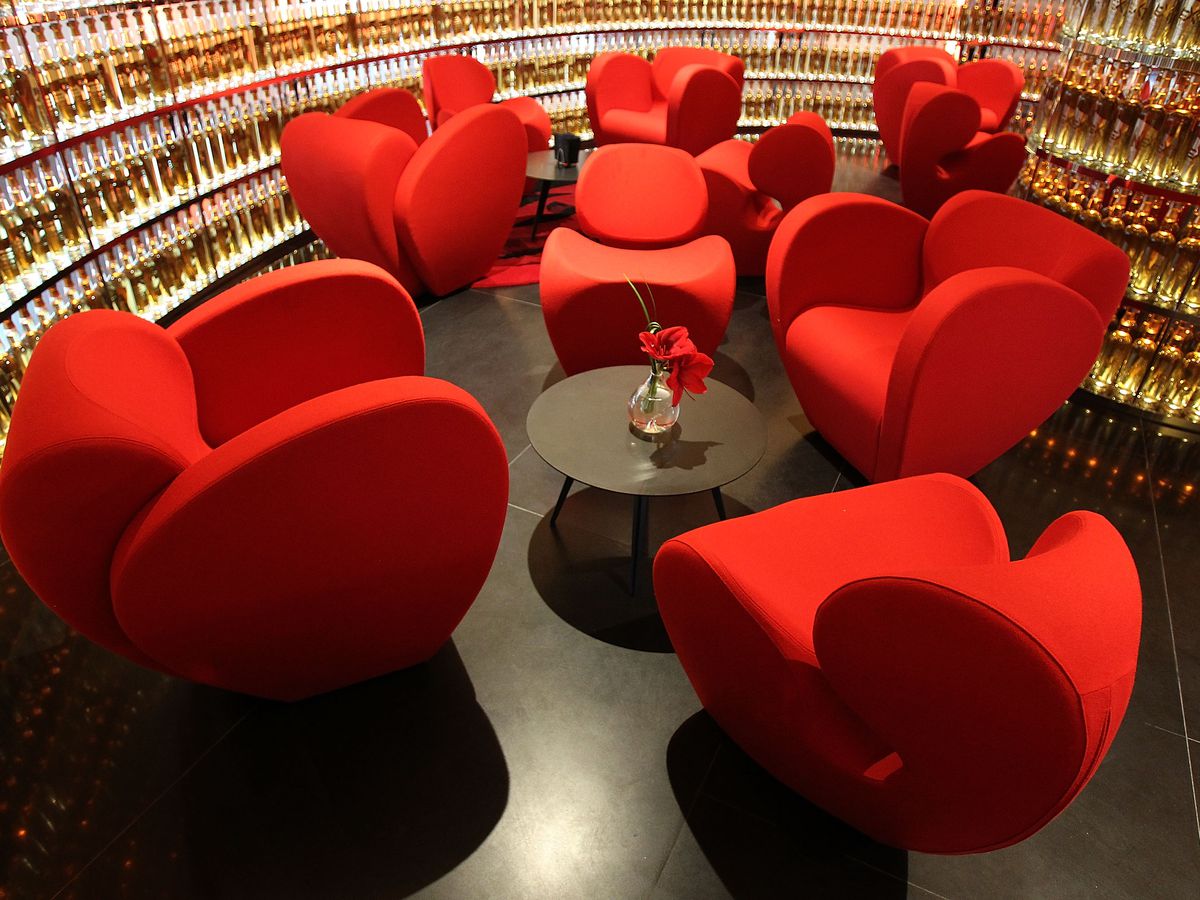 Red plush seating next to a backlit angular wall of whiskey