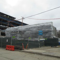 The east front of the media building, still incomplete, but the to-be-used finish brick is visible stacked inside the tarps -