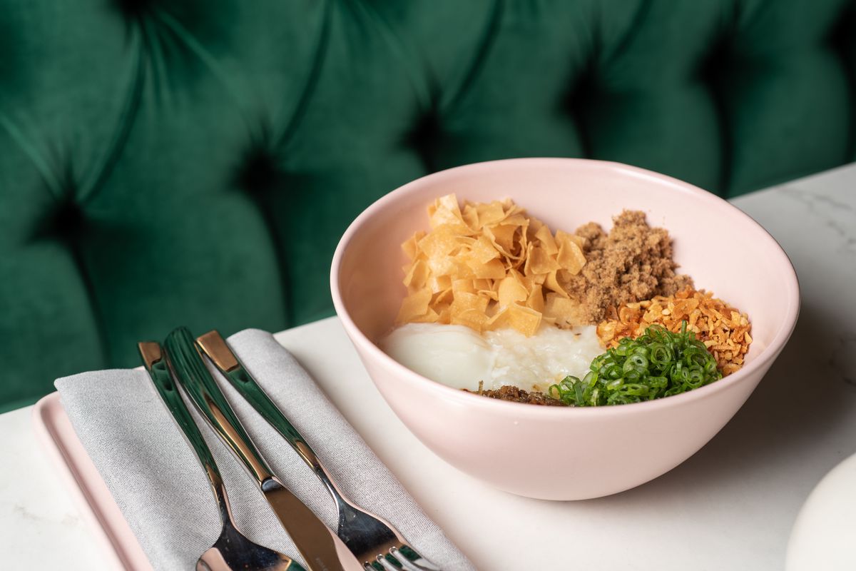 At Nightshade in Los Angeles, chef Mei Lin serves congee in a pink bowl, photographed on a marble table in front of a green tufted banquette.