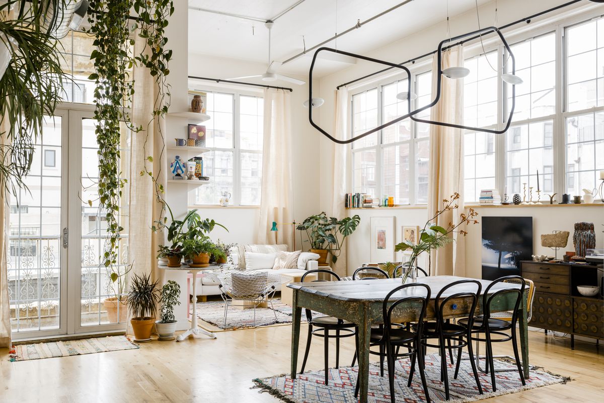 一个明亮的居住空间，有一张旧餐桌，周围是黑色椅子和奶油沙发。可以在餐桌上，侧桌子上找到植物，并从天花板上悬挂。