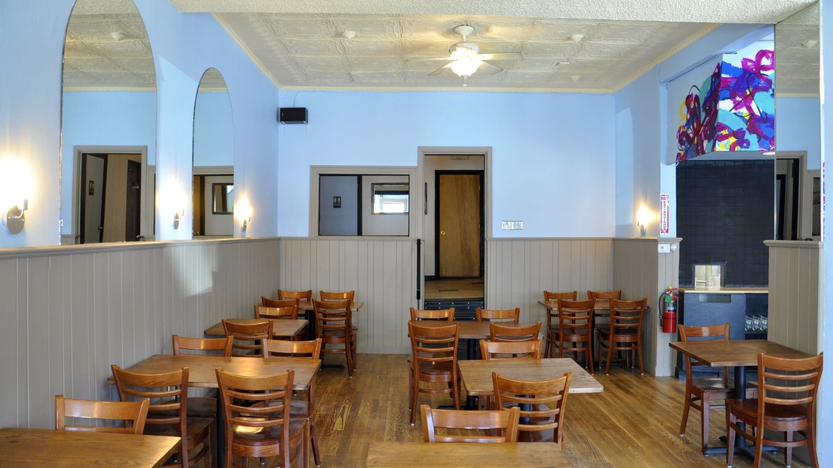 Wide view of a restaurant space with wooden floors and tables, tan-colored wood paneling on the lower half of the walls and light blue-painted walls above