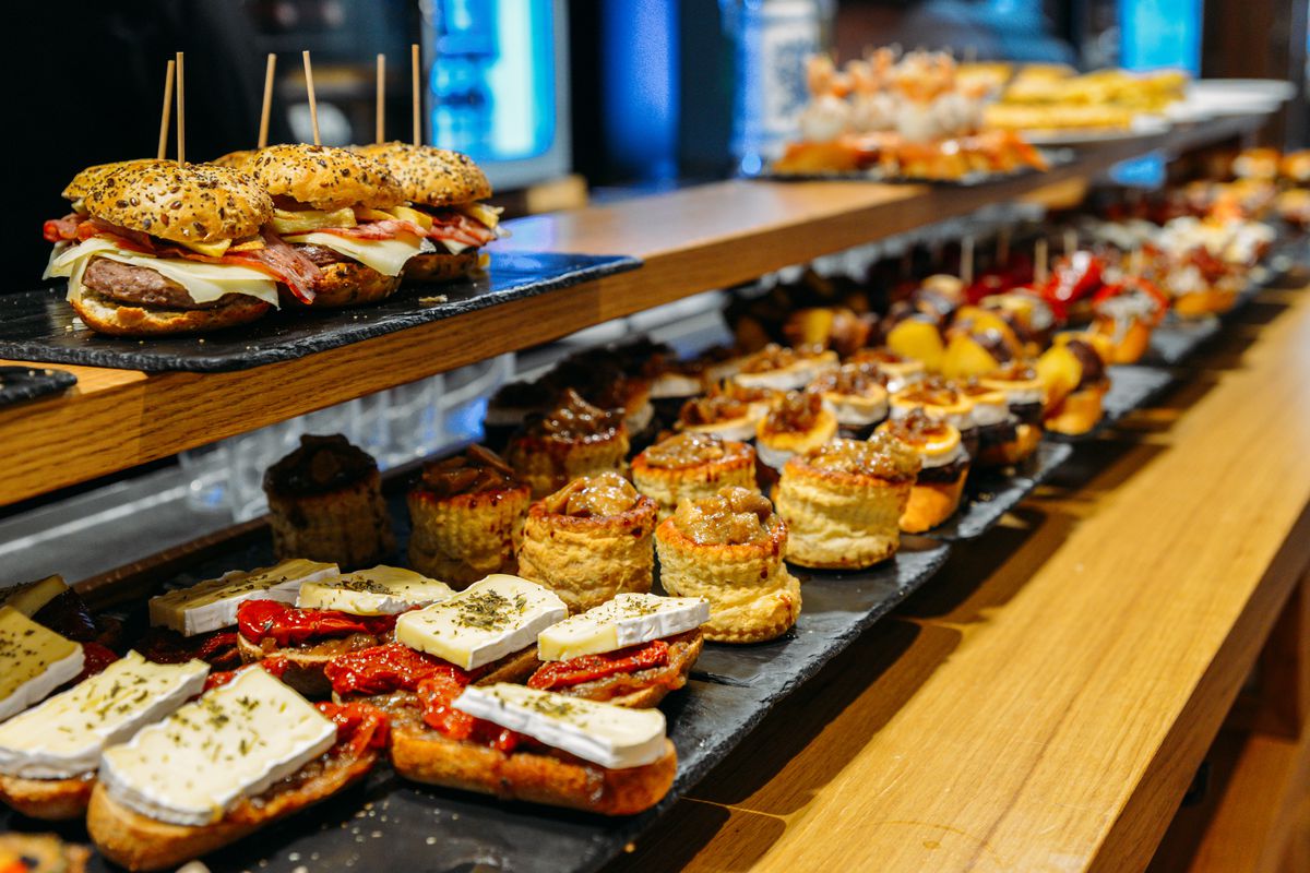Pintxos piled on slate trays atop a wooden table 