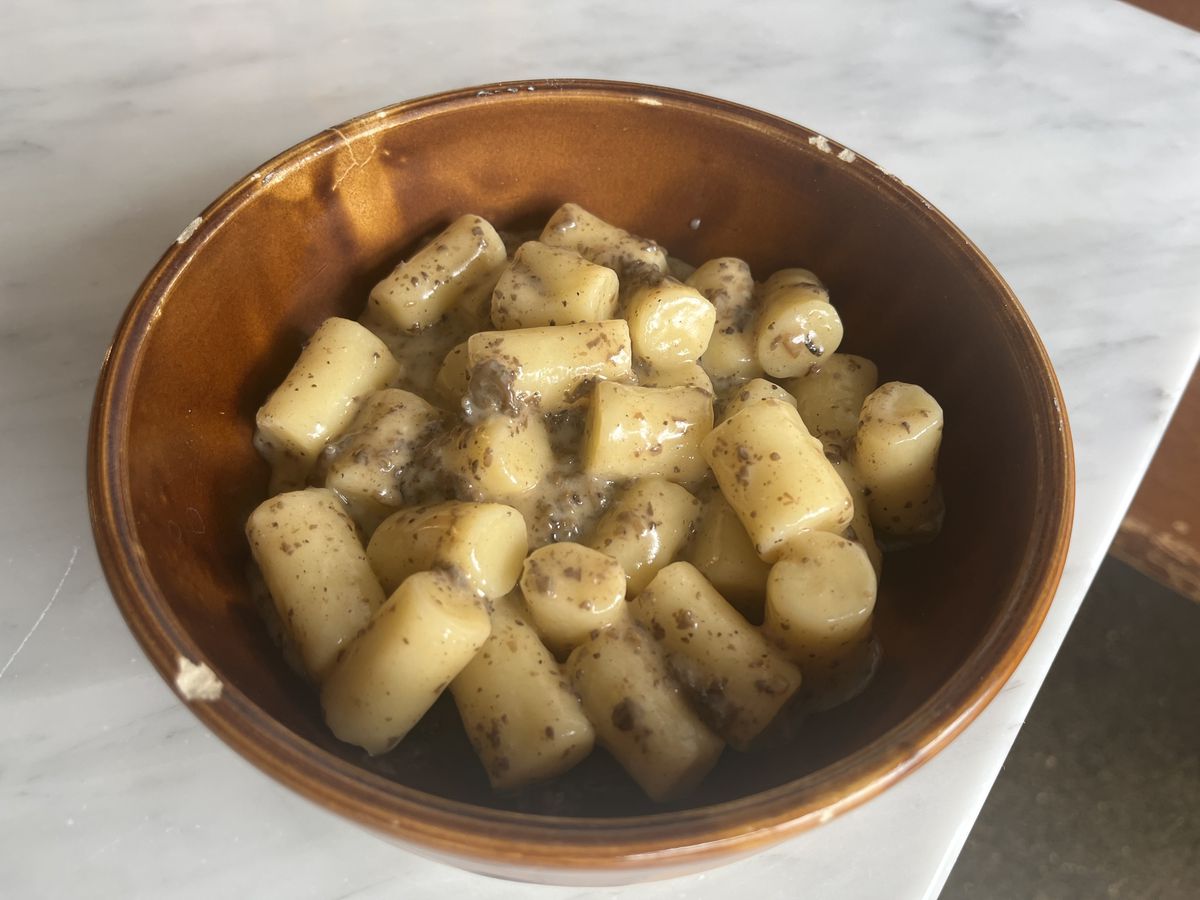 Tubes of gnocchi in a rich yellow sauce presented in a brown bowl. 