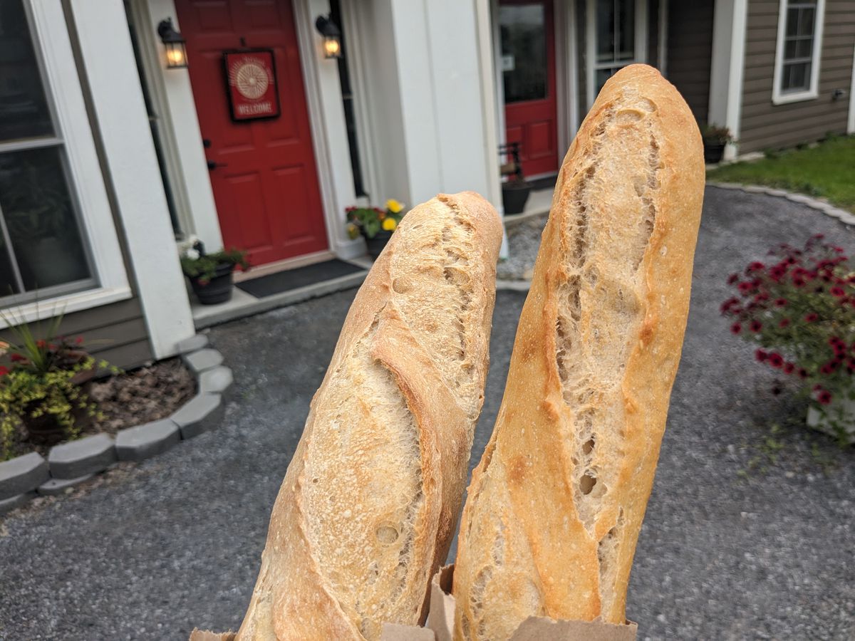 Two loaves of bread held up before a red door.