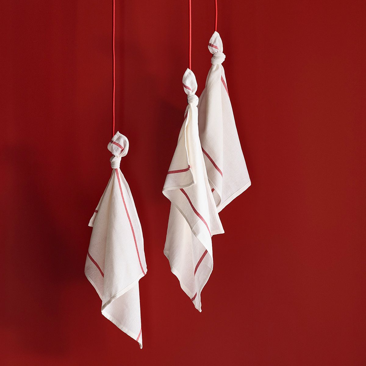 Three white kitchen towels hang on a red wall. 