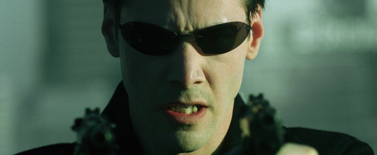 Neo holds two pistols while wearing sunglasses in The Matrix