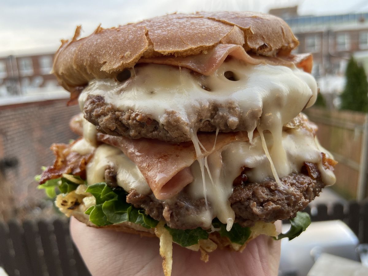 A hand holds a very stacked burger, with all the fixin’s.