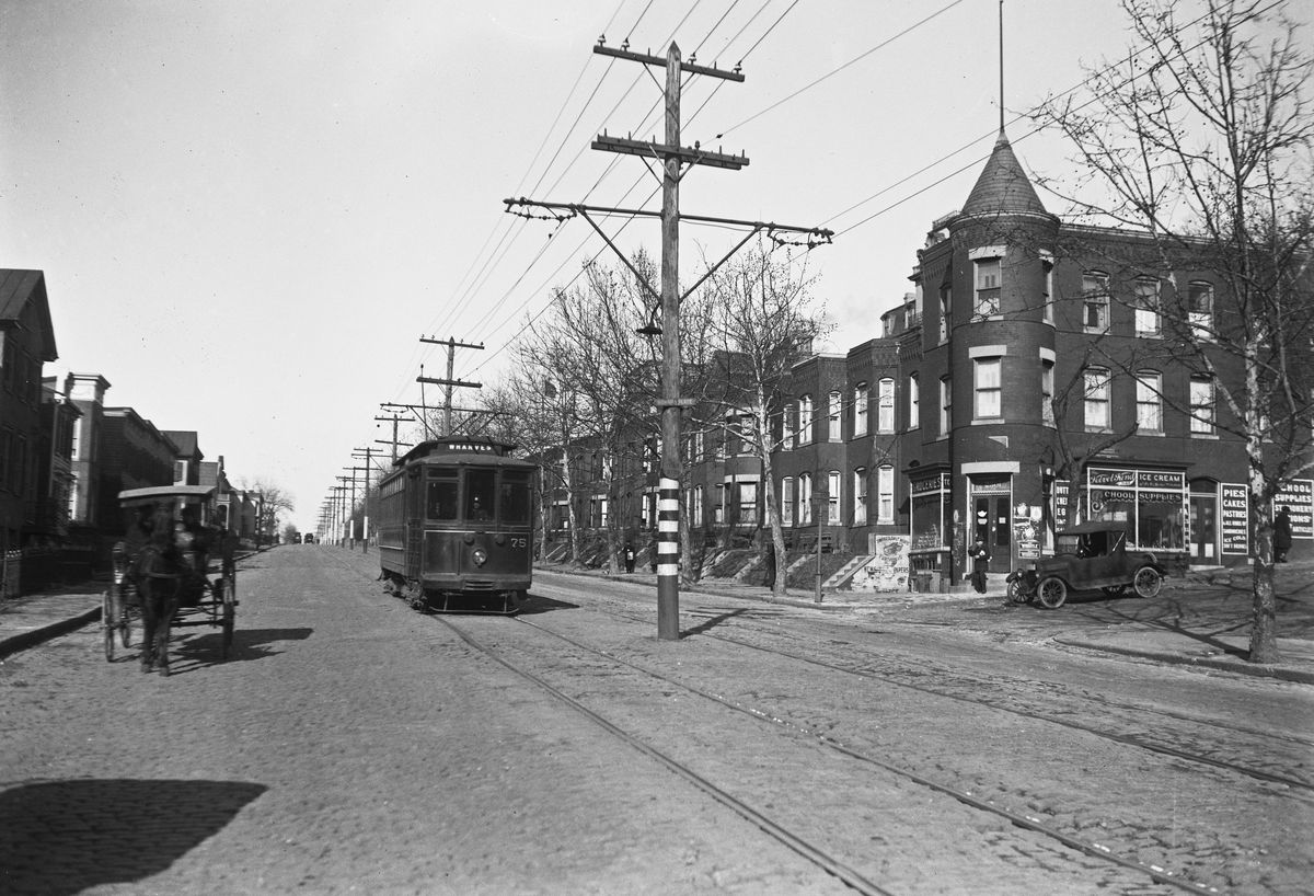 A black-and-white photo of a dense residential street with a streetcar running down the center.