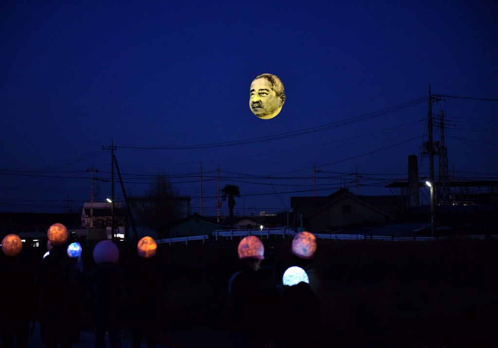 A large balloon (top) of a face of “ojisan”, a middle aged man, is illuminated with LED lights as it floats above the grounds of Nishiki elementary school in Utsunomiya in Tochigi prefecture, 100km north of Tokyo. Members of art group “Me”, meaning “eye” 