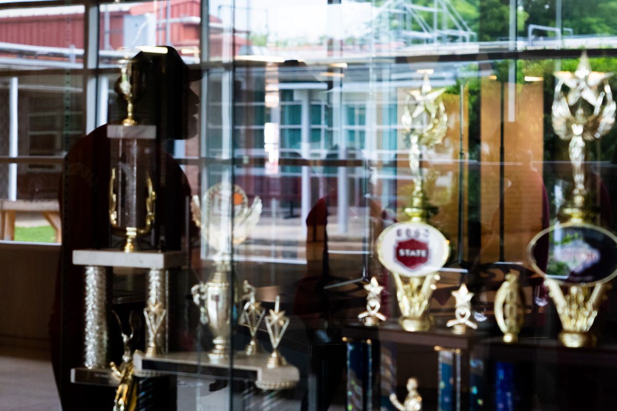 A table full of trophies sits in front of a person in silhouette 