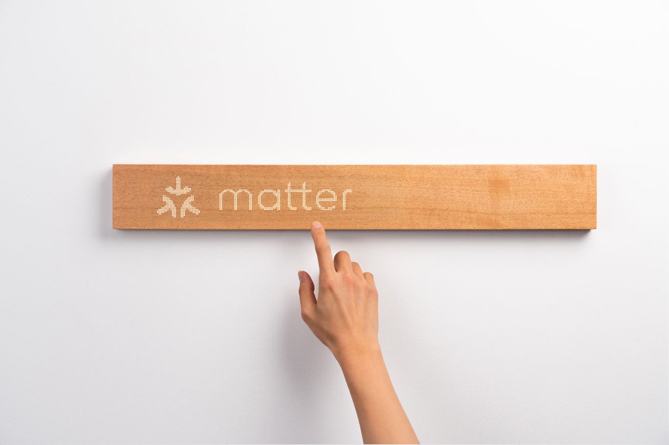 A piece of wood with a a Matter logo on and a hand reaching to touch it.