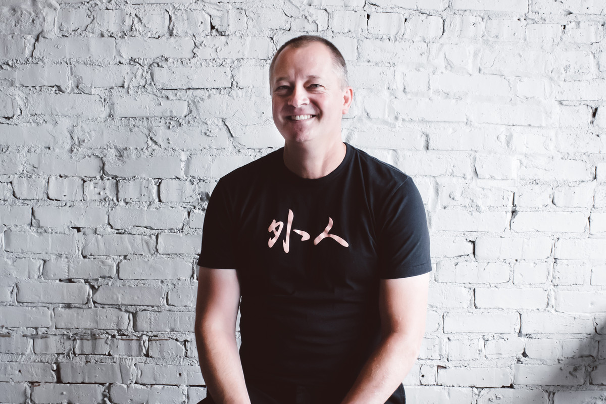 A portrait of a chef wearing a black T-shirt and jeans.