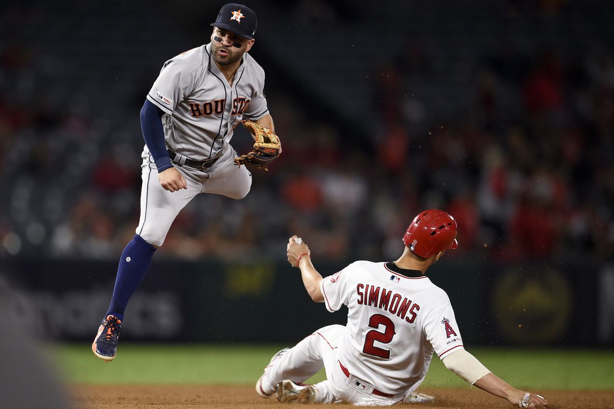 Jose Altuve jumps to avoid the slide of Andrelton Simmons during a force out at second base.  Simmons is wearing the white uniform with red trim.  Altuve is wearing the gray uniform with blue trim.