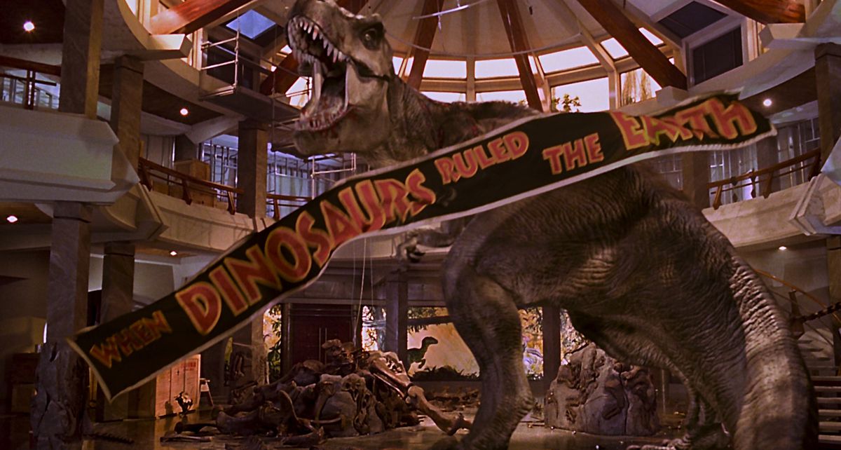 jurassic park ending: the t-rex defeats the raptors in the jurassic park lobby as a “when the dinosaurs ruled the earth” banner falls from the ceiling