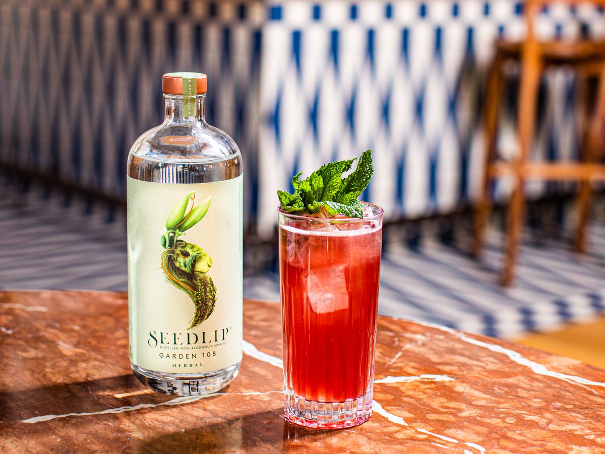 A bright red cocktail garnished with herbs, and a glass bottle of Seedlip Garden 108.