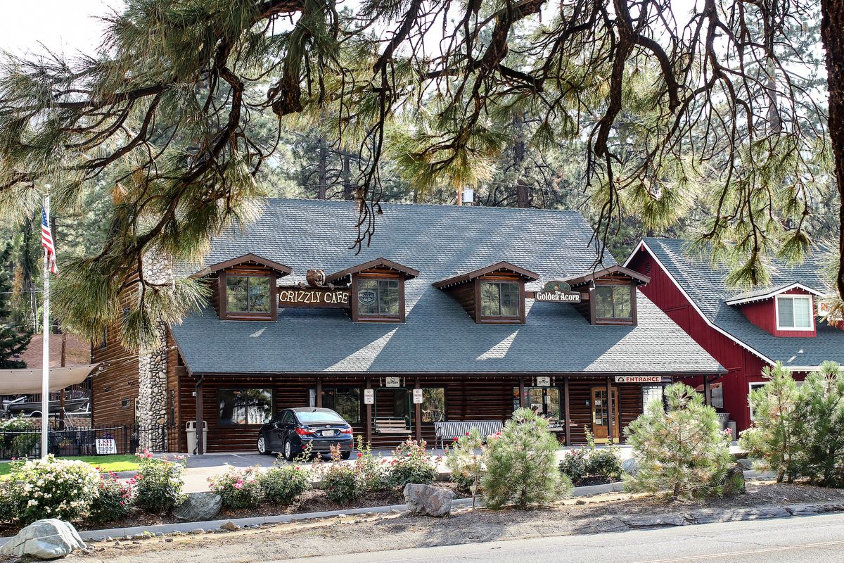 A woodsy fake log cabin stands as a restaurant surrounded by pine trees.