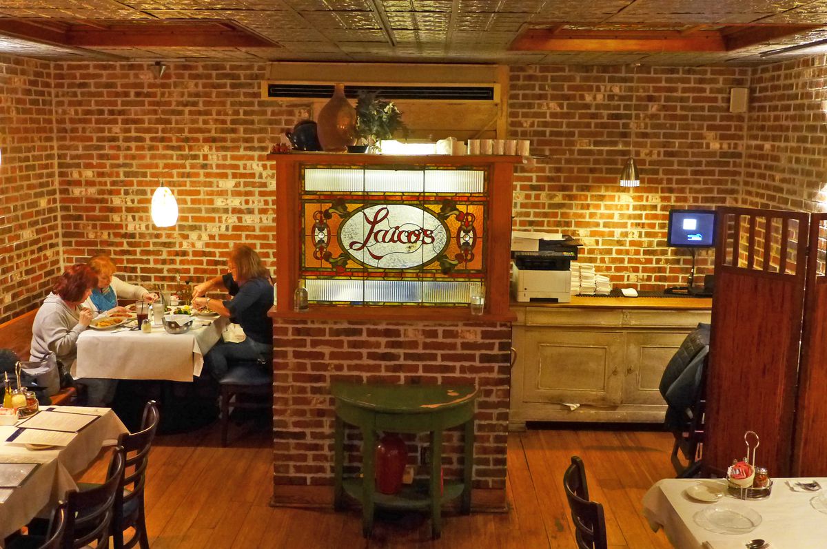 A brick wall room with a table seated in the left rear corner, and a backlit sign with the name of the restaurant.