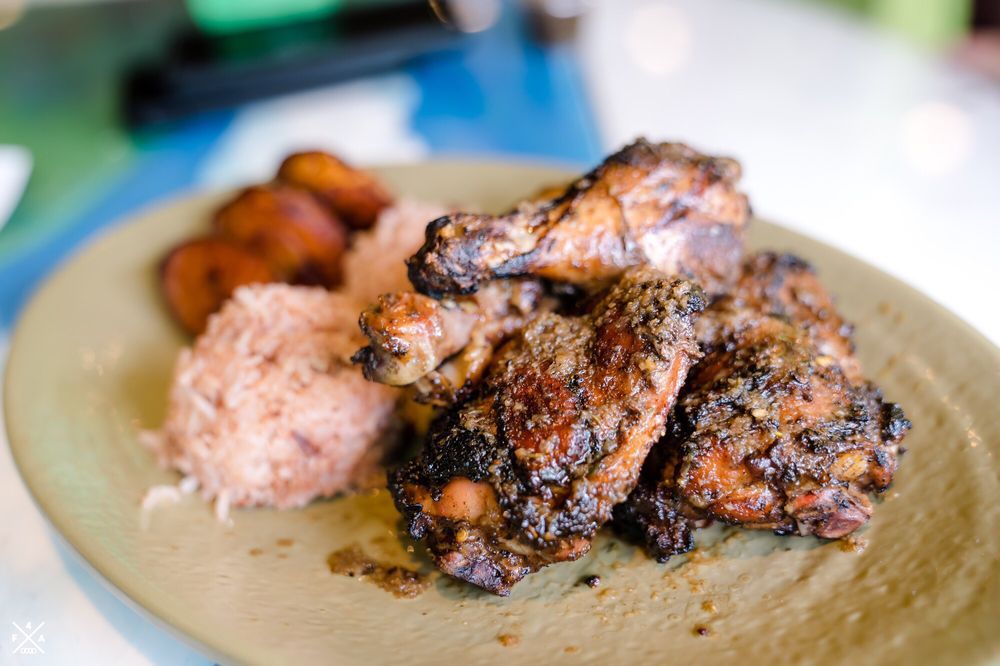 A close-up shot of jerk chicken with rice in the background.