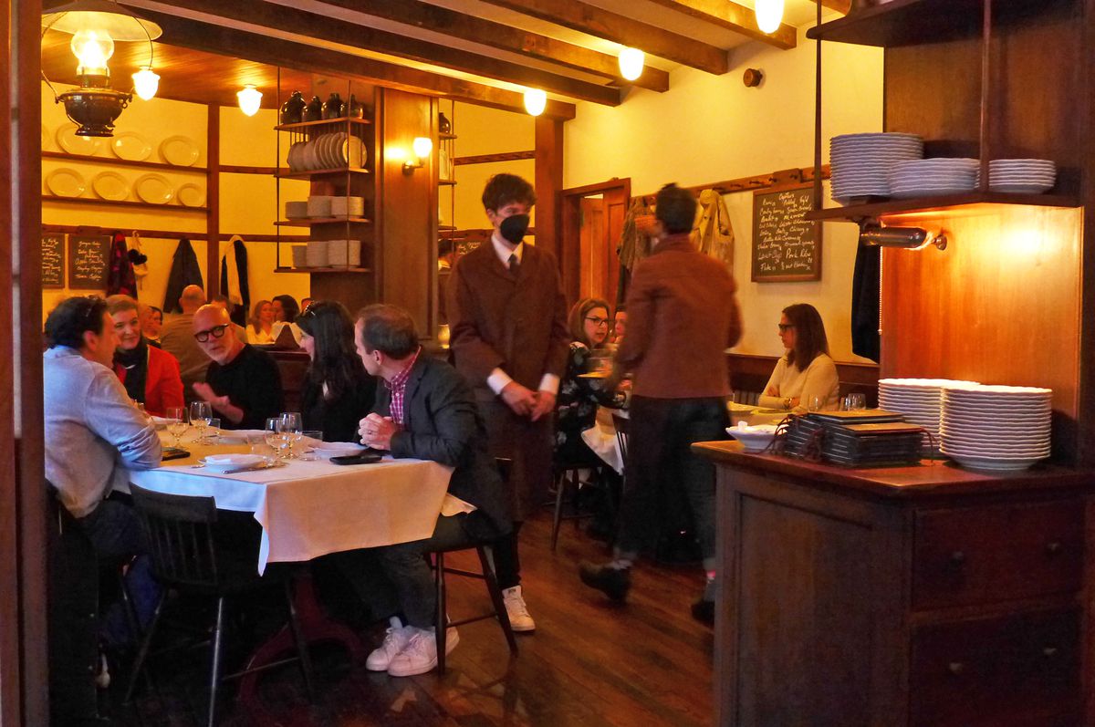 A dining room with dim lighting and waiters wandering around in dark red shopcoats.