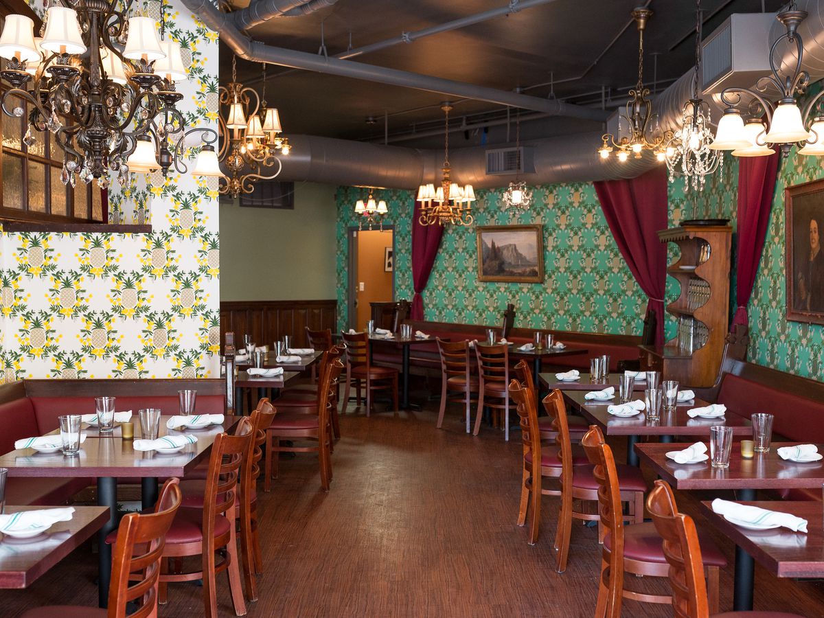 A restaurant interior features two different eye-catching wallpapers; one is white with a yellow and green pineapple pattern, and the other has teal and gold diamonds. Red velvet curtains hang in several places.